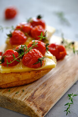 Fried slices of fresh bread with cheese and cherry tomatoes on a wooden board on a gray background. T
