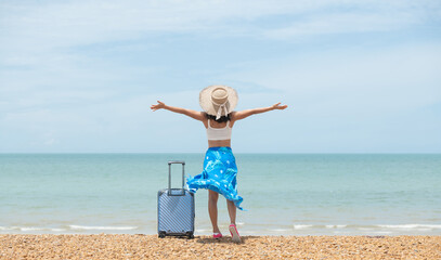 Beautiful young woman with a hat standing with suitcase on the wonderful sea background, concept of...
