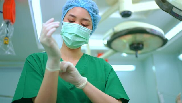 Portrait of Asian surgeon with medical mask standing and wearing medical gloves in operation theater at a hospital. Team of Professional surgeons. Healthcare, emergency medical service concept
