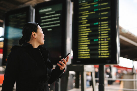 Businesswoman with smart phone looking at departure board