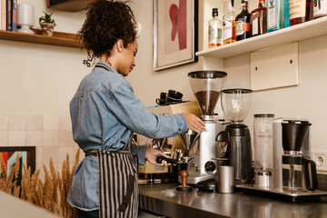 Young black barista wearing apron making coffee while working in cafe