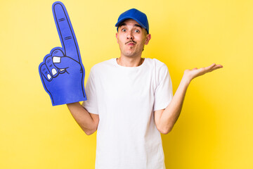 young hispanic man feeling puzzled and confused and doubting. number one fan concept