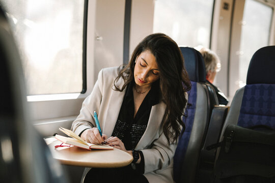 Businesswoman writing in diary while sitting by train window