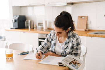 Young woman doing homework while sitting at table in kitchen