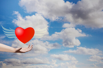 Obraz na płótnie Canvas Hand holding heart shape with wings on blue sky. Valentine decorative symbol concept. 3D rendering image.