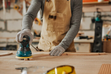 Close up of young carpenter sanding wood while building handcrafted furniture in workshop, copy space