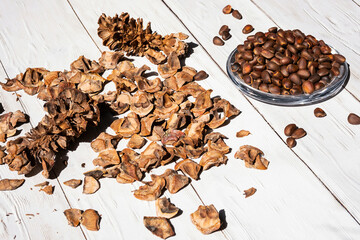 Cedar cones, unshelled pine nuts in glass bowl on white wooden table.