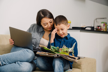 Asian woman and her son sitting at couch and playing with book at home