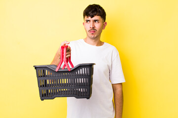 young hispanic man feeling sad, upset or angry and looking to the side. empty shopping basket concept