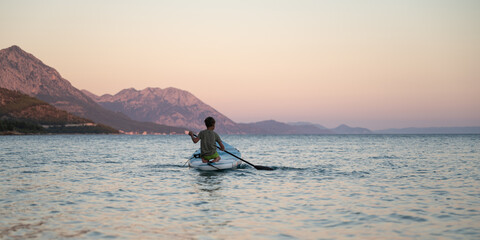 View from behind of a boy paddling on sup board on the sea