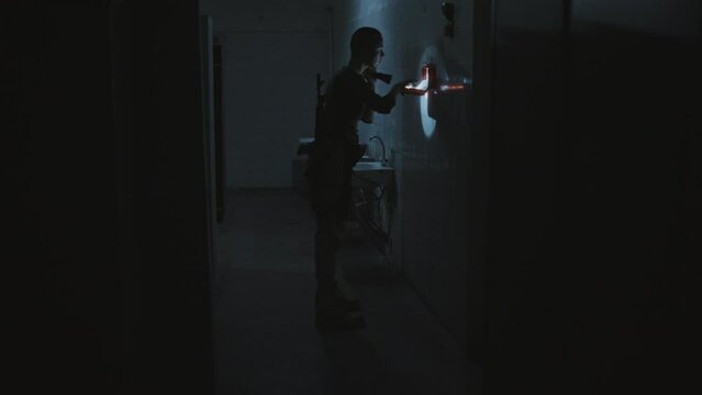 Wide shot of female soldier with shaved head walking in abandoned dark public bathroom with lights flickering, searching first aid kit