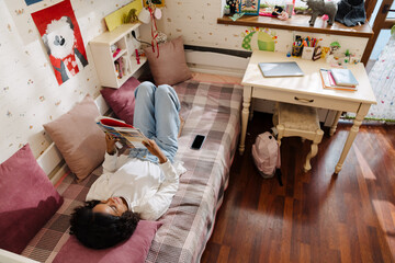 African smiling teen girl liying on bed with book
