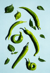 Fresh green chilli peppers with green leaves flat lay on blue background. Creative, minimal food layout.