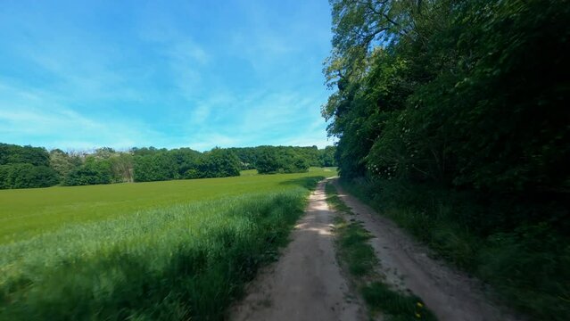 FPV DRONE SHOT - Flight above a dirt road and over the green field