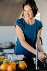 White mature woman washing fruits while cooking in kitchen
