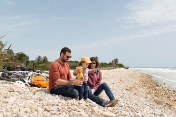 Couple with her little daughter at a pebble beach with their bicycles behind them. Low-footprint transportation.