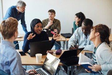 Multiracial students discussing with each other while sitting in classroom