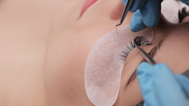 Eyelash extension procedure. The working process of professional beauty master lengthening female lashes. Fake eyelashes. Eyelashes extensions close up. Makeup artist and client in beauty salon.