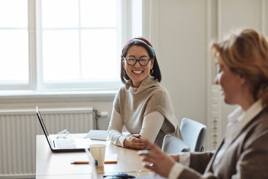 Cheerful female professor looking at colleague sitting in staffroom