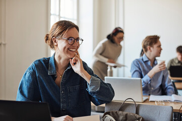 Happy female student with eyeglasses looking away while sitting in classroom