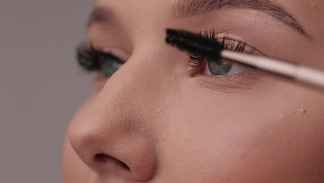 Close up portrait of woman face. Young, beautiful girl with fresh soft skin combing long black eyelashes with special mascara brush. Fake eyelashes. Eyelashes extensions close up.