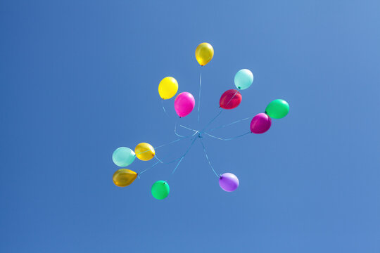 Balloons of red, burgundy, pink, purple, yellow, blue and green colors with ribbons, in a blue clear sky, without clouds, during the day.