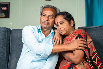 Senior man consoles by embracing his thouhgtful wife at home while on sitting sofa - concept of...