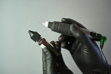 hands in black leather gloves hold a tattoo machine and tattoo paint in their hands. tattoo. Permanent makeup