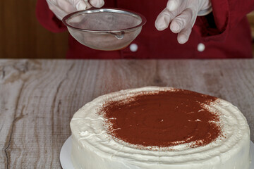 Confectioner decorates white cream cake cocoa powder