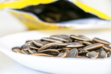 Close up of nutritious roasted sunflower seeds on a white plate poured from bag, ready to snack, healthy eating concept