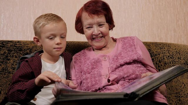 A happy great-grandmother and a little grandson look at a large photo album together and laugh.