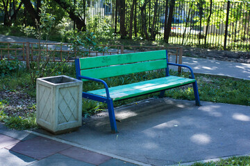 Green and blue bench and trash can near paths