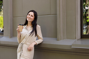 a woman smiles with a craft cup to take away in town on a walk.