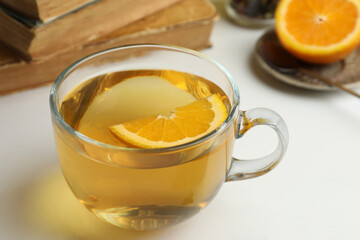 Glass cup of freshly brewed tea with orange on light table, closeup