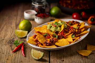 Delicious plate of yellow corn nachos chips with cheese, minced meat and red hot spicy salsa over wooden table