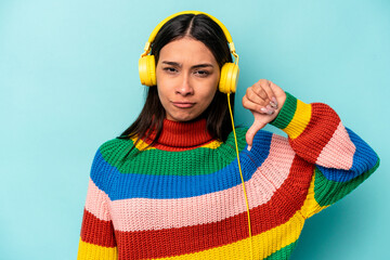 Young hispanic woman listening to music isolated on blue background showing a dislike gesture,...