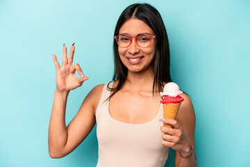 Young hispanic woman holding an ice cream isolated on blue background cheerful and confident...