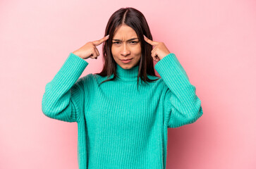 Young hispanic woman isolated on pink background focused on a task, keeping forefingers pointing head.