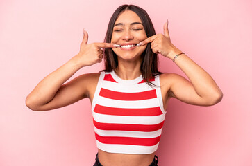 Young hispanic woman isolated on pink background smiles, pointing fingers at mouth.