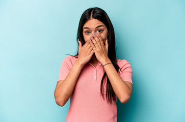 Young hispanic woman isolated on blue background shocked covering mouth with hands.