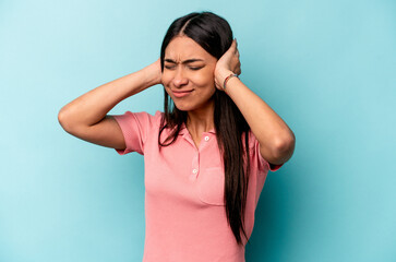 Young hispanic woman isolated on blue background covering ears with hands.