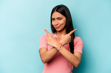 Young hispanic woman isolated on blue background points sideways, is trying to choose between two...
