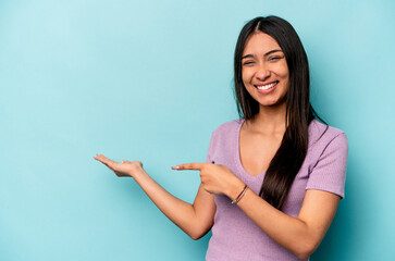 Fototapeta Young hispanic woman isolated on blue background excited holding a copy space on palm. obraz