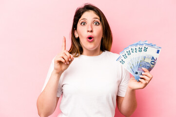 Young caucasian woman holding banknotes isolated on pink background having some great idea, concept of creativity.