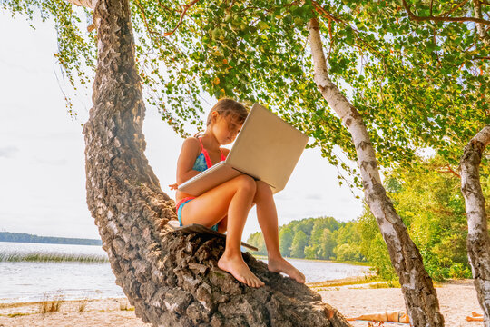 Young Child Girl Having A Video Chat Through Laptop On The Sea Beach. Summer Vacation Concept, Studying Online With Tablet, Distance Learning, Self Education, Beach Work