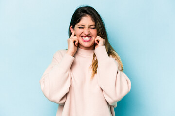 Young caucasian woman isolated on blue background covering ears with hands.