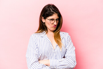 Young caucasian woman isolated on pink background frowning face in displeasure, keeps arms folded.