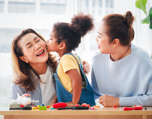 Little mix race granddaughter kissing happy older Asian grandma on the cheek in the living room.  Preschool grandchild girl congratulates happy grandma with mothers day concept