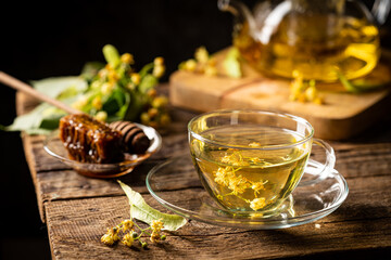 Cup of herbal tea with linden flowers on dark background