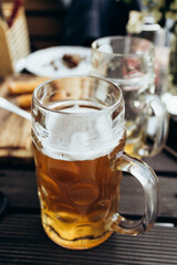 There is a mug of fresh beer on a wooden table in a street cafe